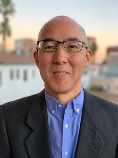 An Asian man in glasses and a suit smiling