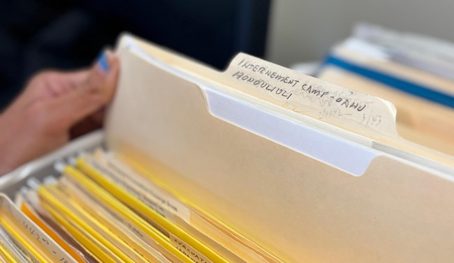 A hand taking a file labeled Honouliuli Internment Camp - Oahu out of a box