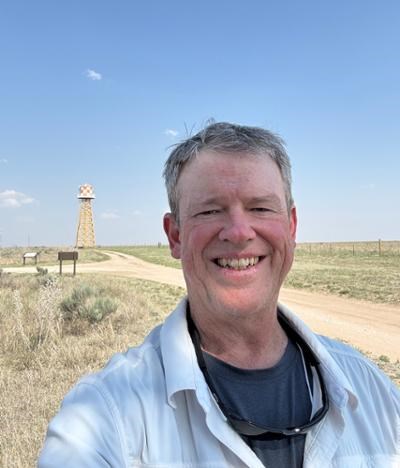 A man smiling with a guard tower recreation in the background
