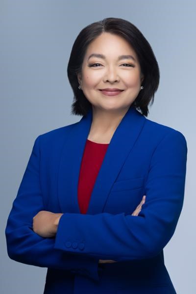 An Asian woman in a blue suit with her arms crossed smiling