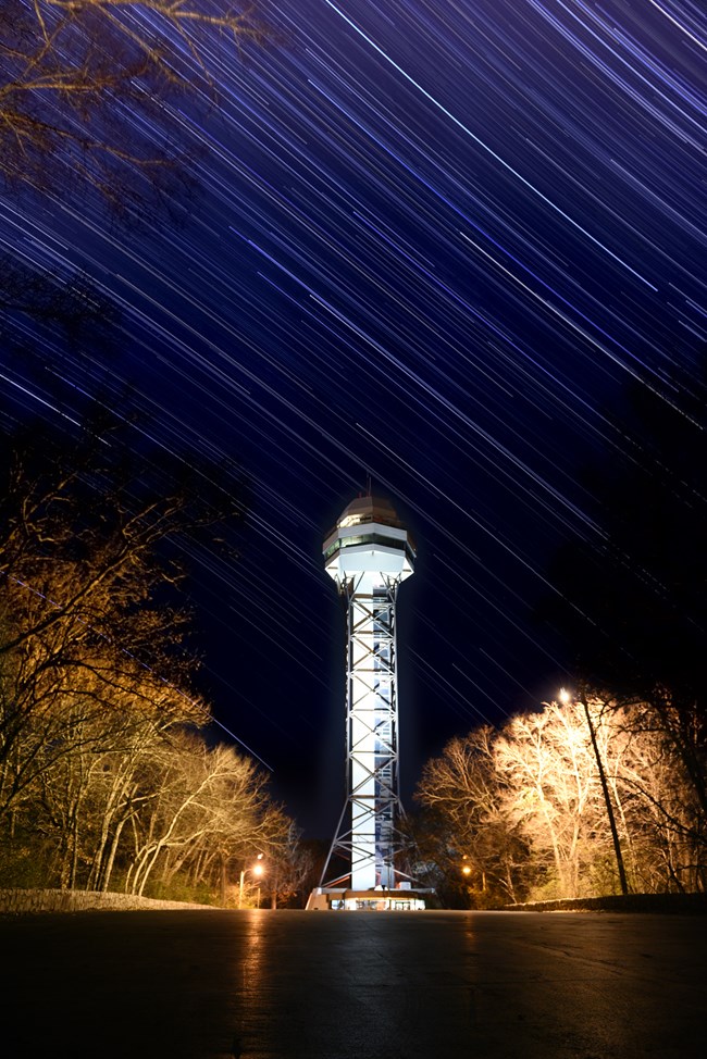 Star lights blur across the night sky. A large white observation tower is in the bottom center of the photo.