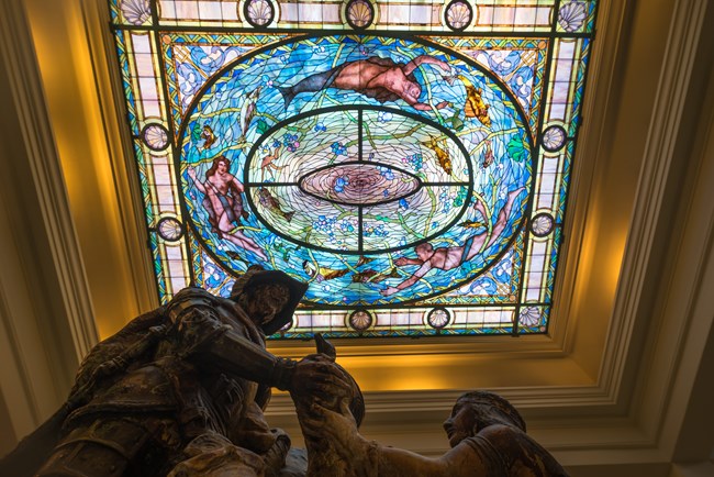 Statue of early explorer and Native American woman under a stained glass ceiling