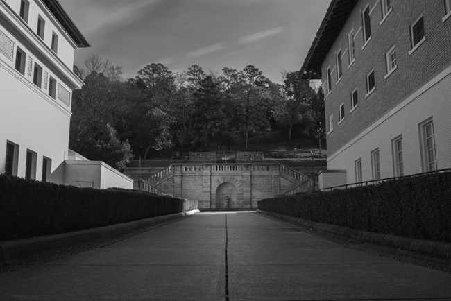 Black and white image of sidewalk in between two bathhouses and in front a stone staircase