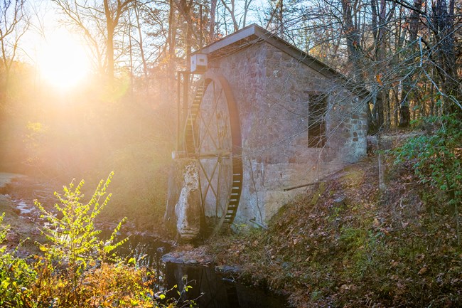 Water wheelhouse with sun setting through the forest