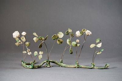 ceramic sculpture with high-fire wire, white clover flowers and green leaves spaced along a connected base.