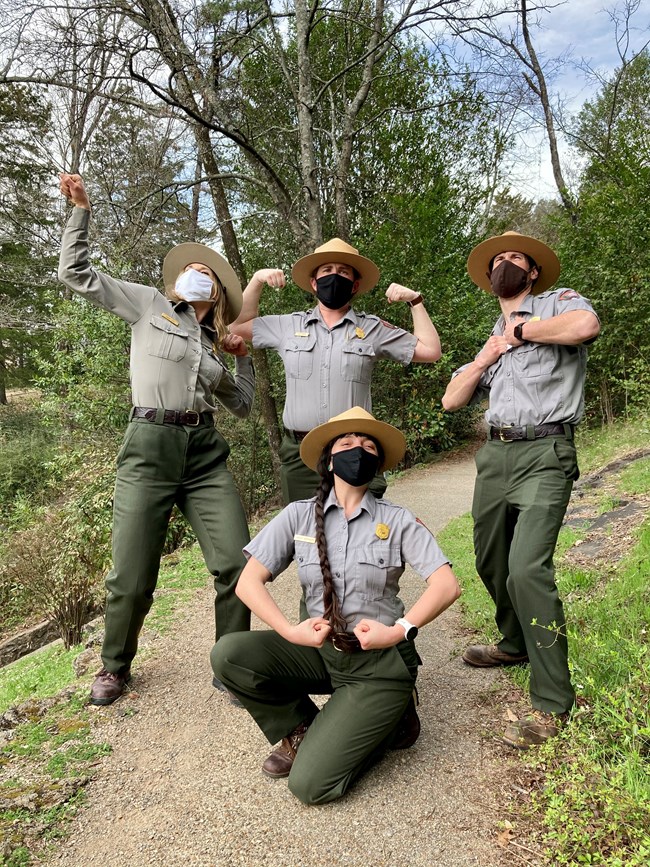 Five park rangers in uniform pose to show off their muscles.