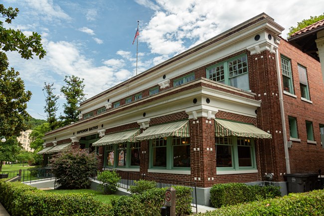 Two story, red brick Superior Bathhouse. Building has large windows on the first floor that are shaded by green and white awnings.