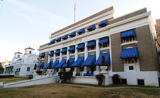 Buckstaff Bathhouse as viewed from the Magnolia Promenade. The three story building features taupe colored brick and white exterior trim, with blue canvas awnings over the windows. Buckstaff Bathhouse as viewed from the Magnolia Promenade. The three story building features taupe colored brick and white exterior trim, with blue canvas awnings over the windows.