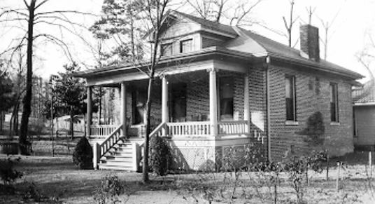 A wooden house with steps leading to a big front porch supported by 4 pillars. 2 windows on the side and one above the porch near the roof.