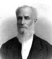 Black and white photo portrait of Hiram Whittington, a white man with a long white beard and a balding forehead. He is wearing a white shirt and a black cardigan.