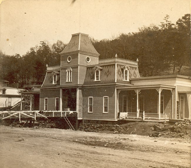 Sepic toned image of the Victorian Hale Bathhouse with a wooden bridge that allows visitors to cross Hot Springs Creek.