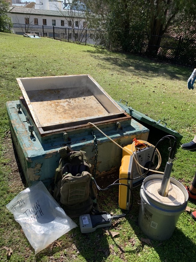 A selection of water testing equipment rests next to an open spring box.