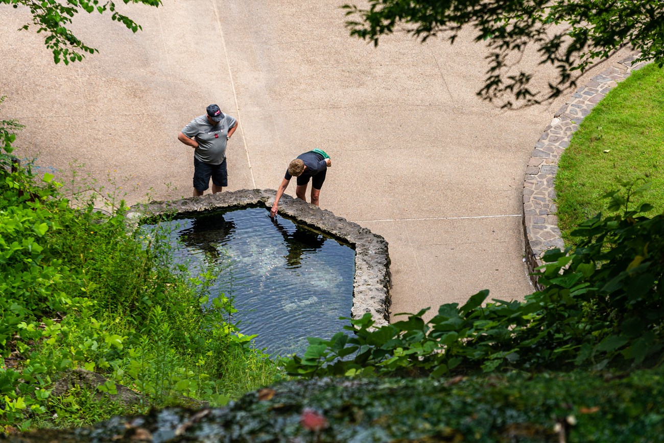 Two adults are bent over touching thermal water in hexagonal pools.