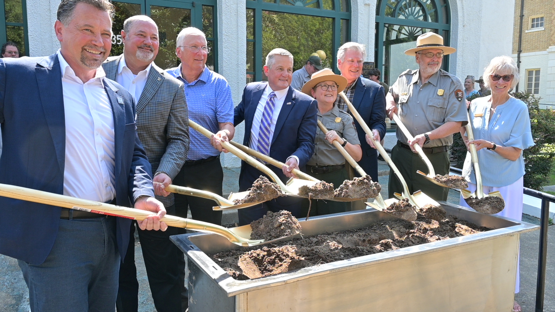 A group of people hold shovels over a tub filled with dirt.
