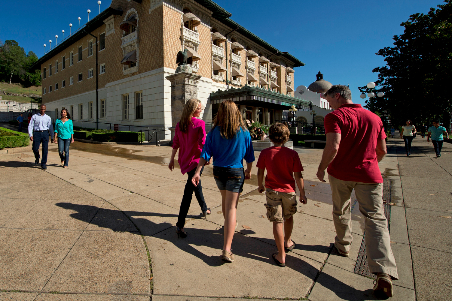 A family of four walks down a sidewalk towards a large ornate 3-story building.