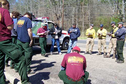 Wildland fire fighters standing around fire leader at briefing