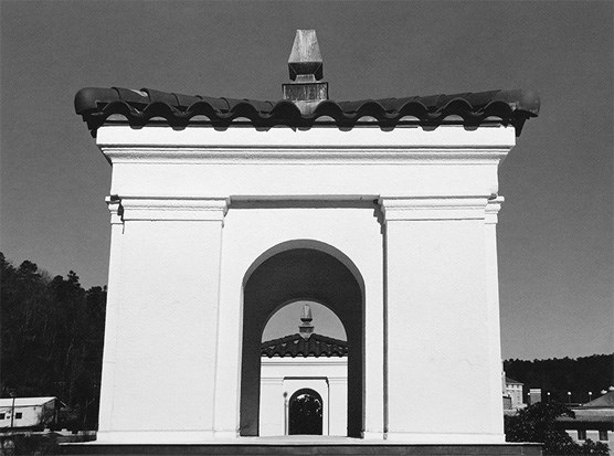 Black and white photo from the Quapaw Bathhouse roof with the nearest tower of the Ozark Bathhouse nearly filling the frame and looking through the arched opening in the Ozark tower, you can see the other Ozark tower. The towers are of white stucco with red tile roofing.