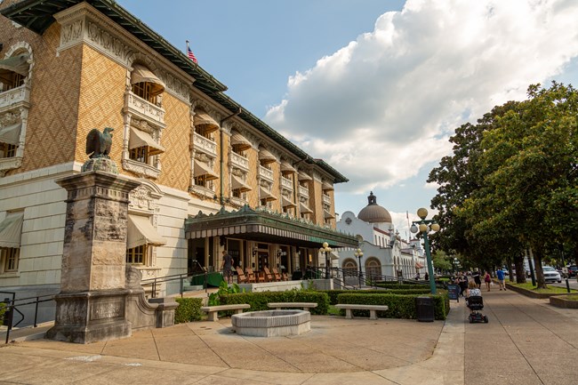 A large ornate multi-story brick building with awnings on all windows and a large green awning over a front porch with chairs.