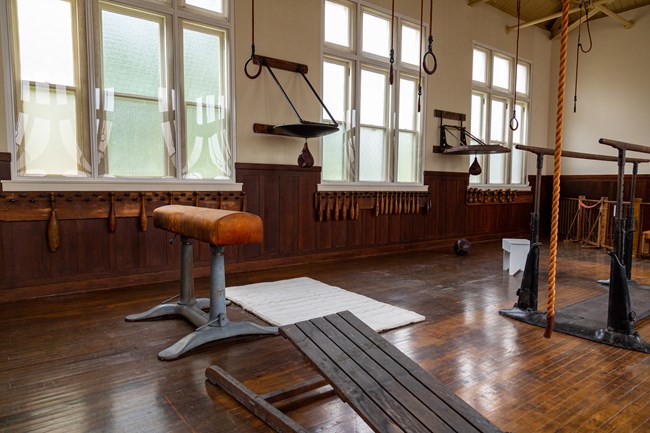 An old gymnasium with all wooden equipment, showing wooden lifting clubs and a climbing rope