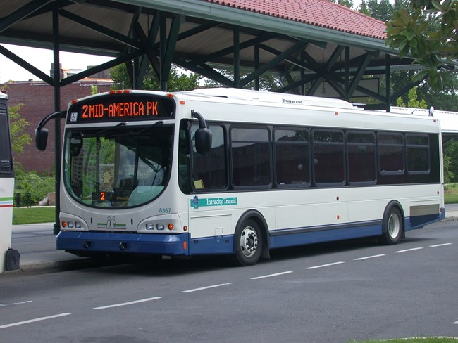 Large intercity bus sits outside the depot. The bus is white with bright blue markings.