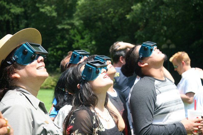 A group of people wearing welding glasses look up