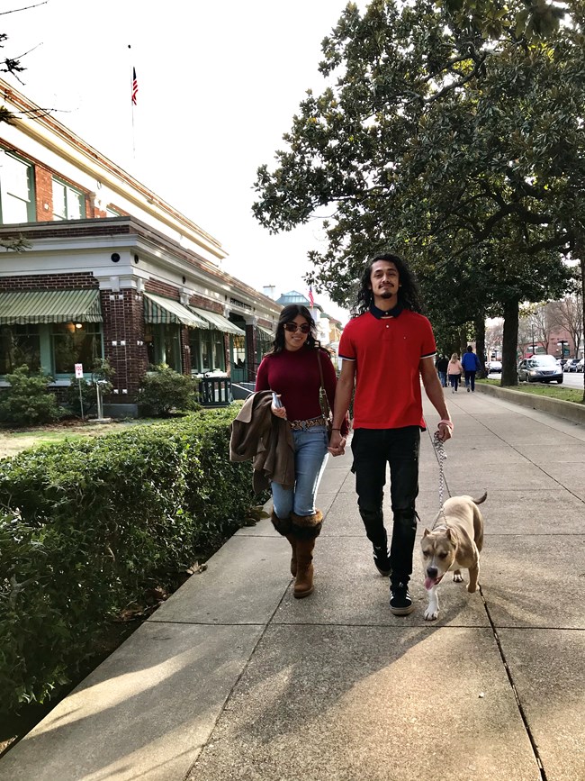 Man and woman walking dog on a leash on the sidewalk