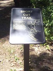 color photo of Shortcut Trail trailhead sign. Sign is made of dark brown metal with gold lettering and map of trail color photo of Shortcut Trail trailhead sign. Sign is made of dark brown metal with gold lettering and map of trail