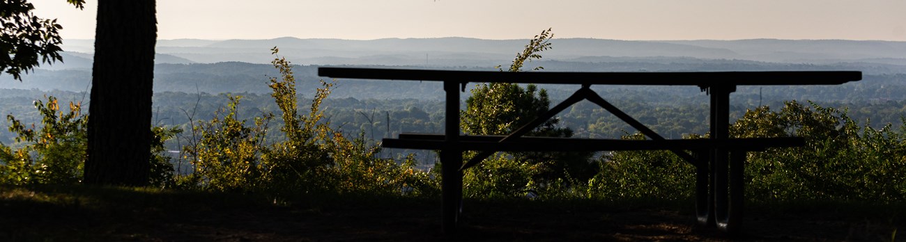 A picnic table in the shade on top of West Mountain with a view of rolling blue hills in the distance
