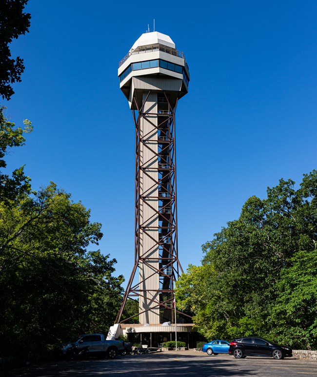 The mountain tower is over ten stories high with a staircase and elevator going up to the top where there is an enclosed lookout are and an exposed balcony over top. It's a very geometric shaped tower its many sharp edges and angles.