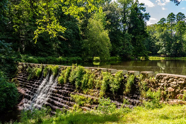 A still pond slowly flows over a terraced dam.