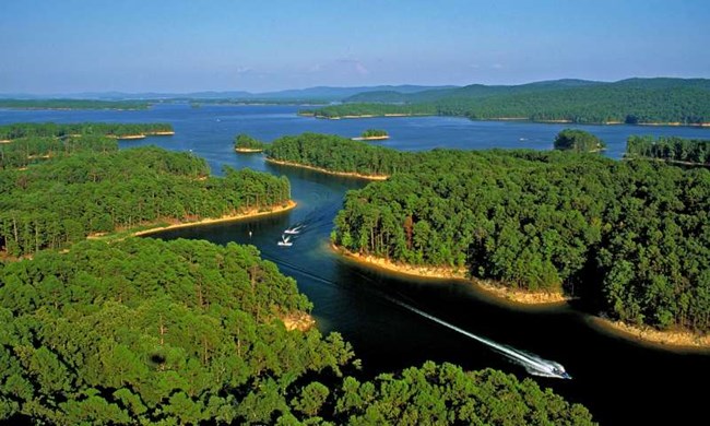 Aerial view of Lake Ouachita with bright blue waters, green forests, and fingered peninsulas.