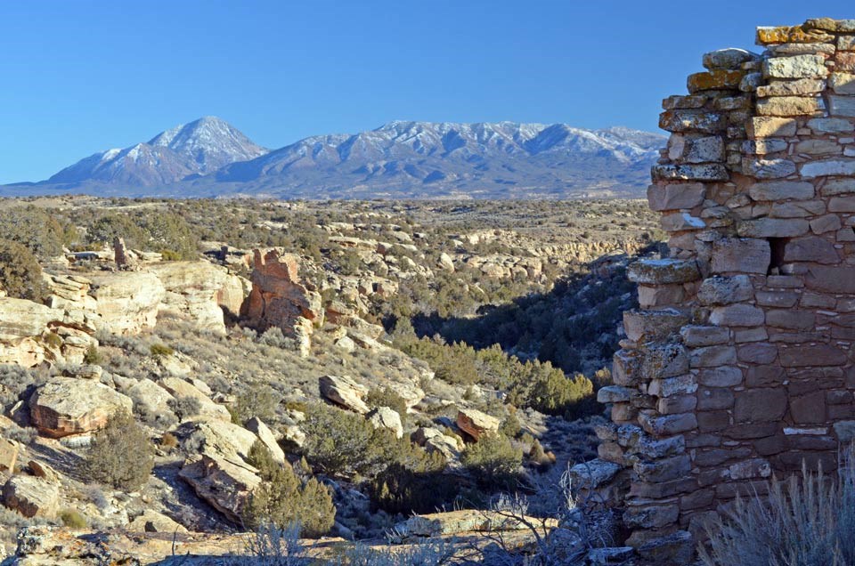 crumbling wall of sandstone ruin with shallow canyon and mountain in the background crumbling wall of sandstone ruin with shallow canyon and mountain in the background
