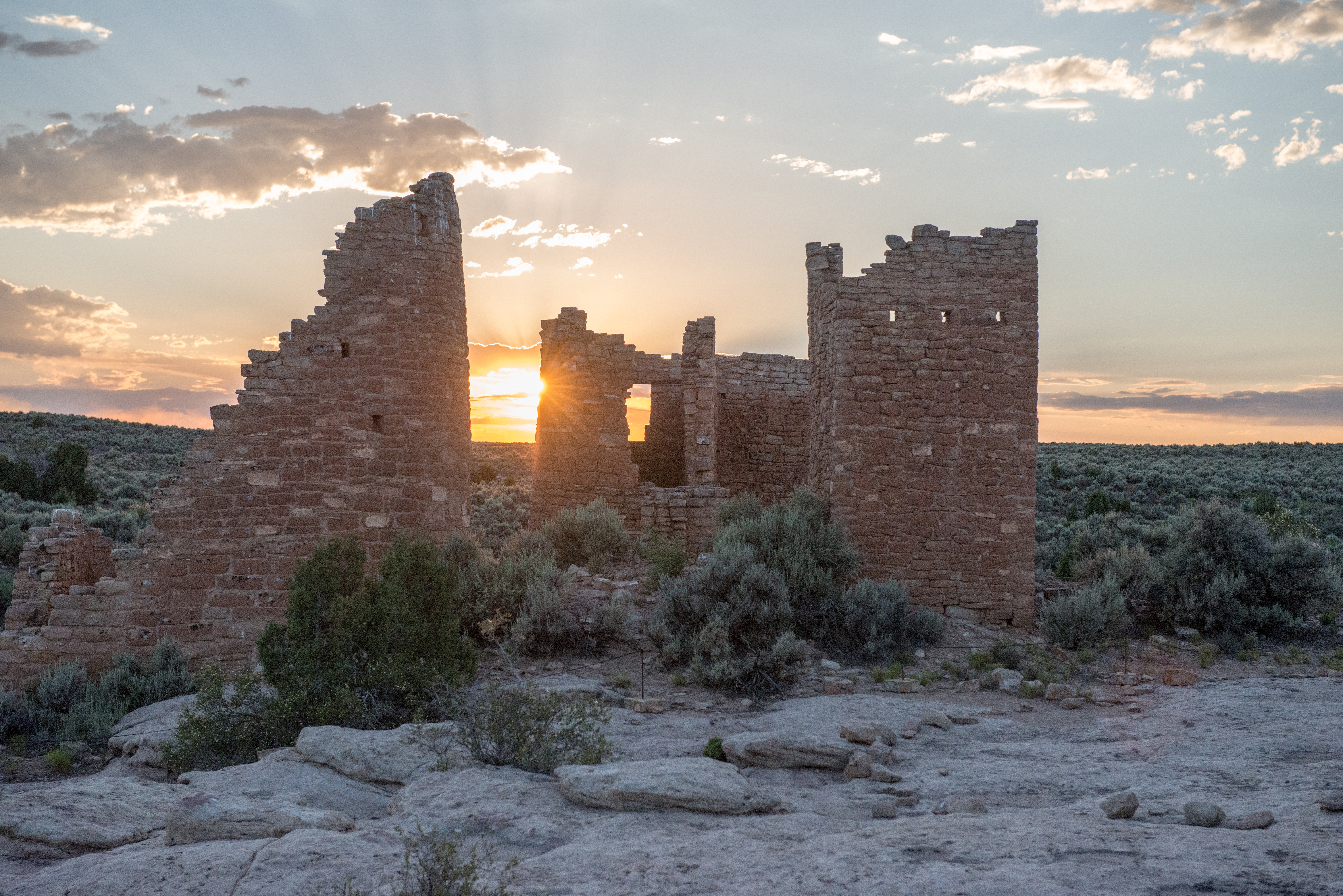 sunset behind eroding stone masonry towers amidst small green shrubs, pale bedrock foreground sunset behind eroding stone masonry towers amidst small green shrubs, pale bedrock foreground