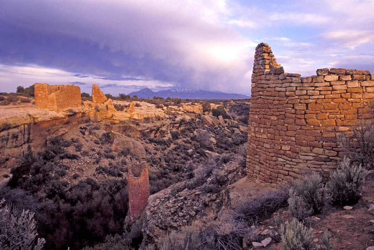 remains of large stone structures around a canyon head, purple sky behind