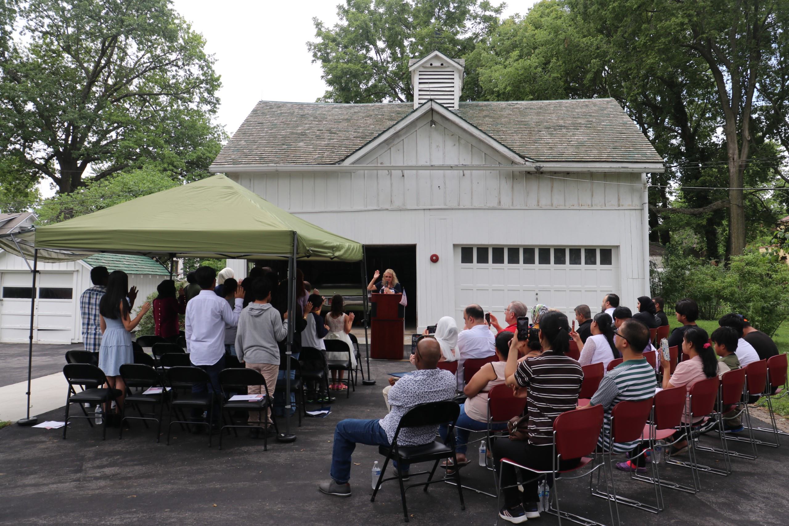 A group of new young citizens take their Oath of Allegiance, their families watch. The Truman garage is in the background, with President and Mrs. Truman's Chrysler showing.