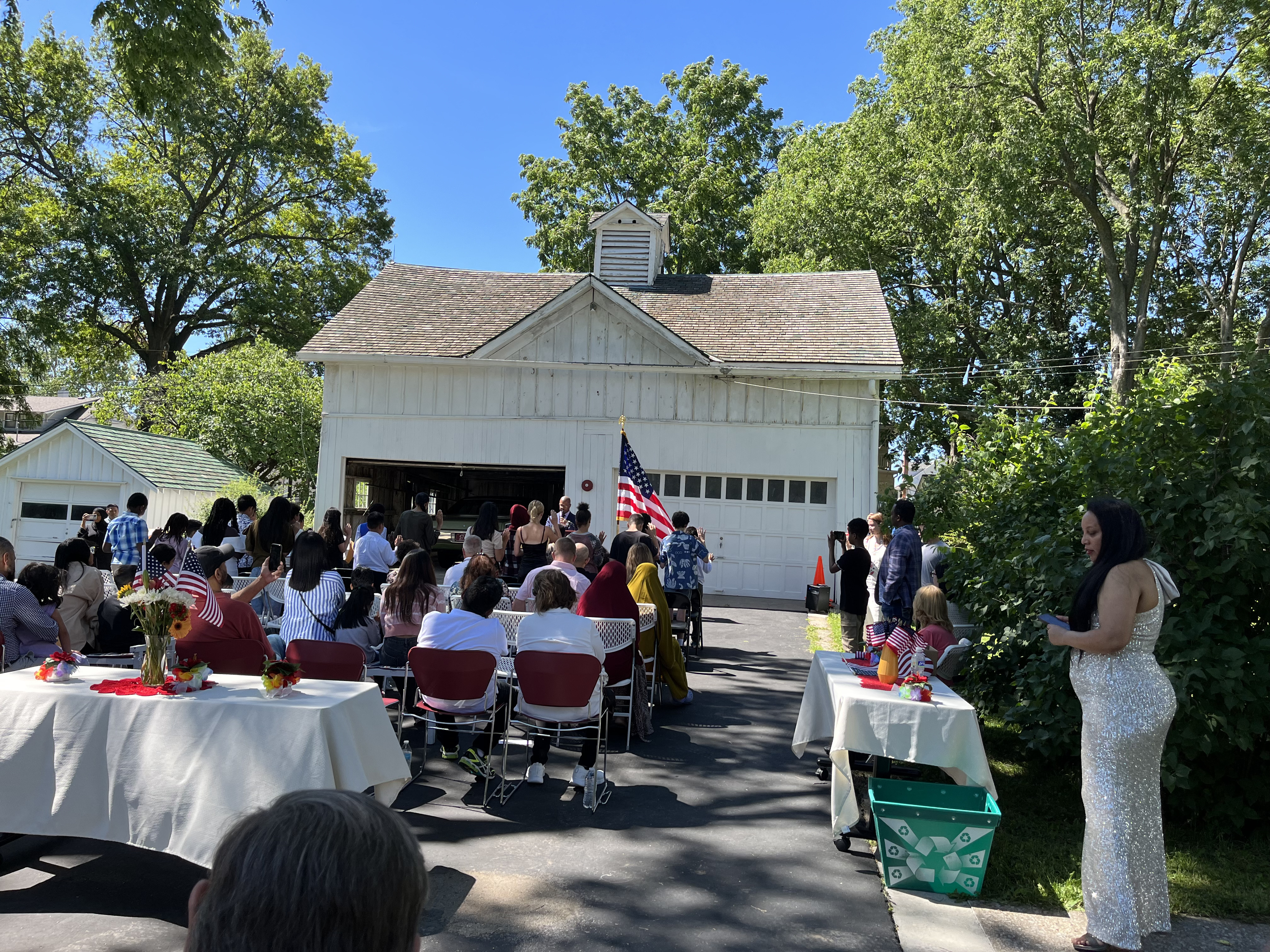 June 10 2024 Naturalization Ceremony at Harry S Truman National Historic Site Naturalization Ceremony A group of young new citizens stand with their right hands raised, families nearby, with the American flag close. President Truman's car is housed in his garage.