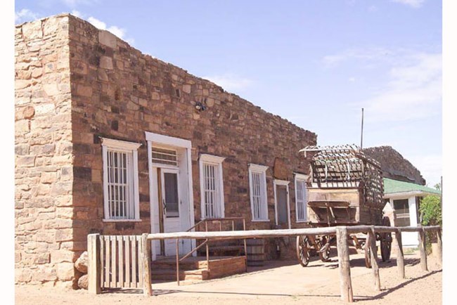 Stone building with a wagon and wooden fence in front.