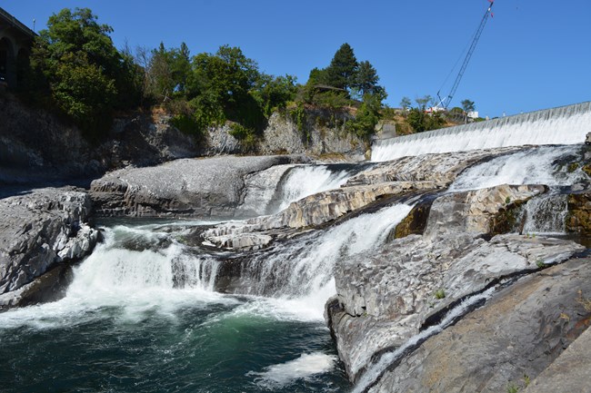 Large grey boulders create a cascading effect on a river, creating a wide white waterfall.