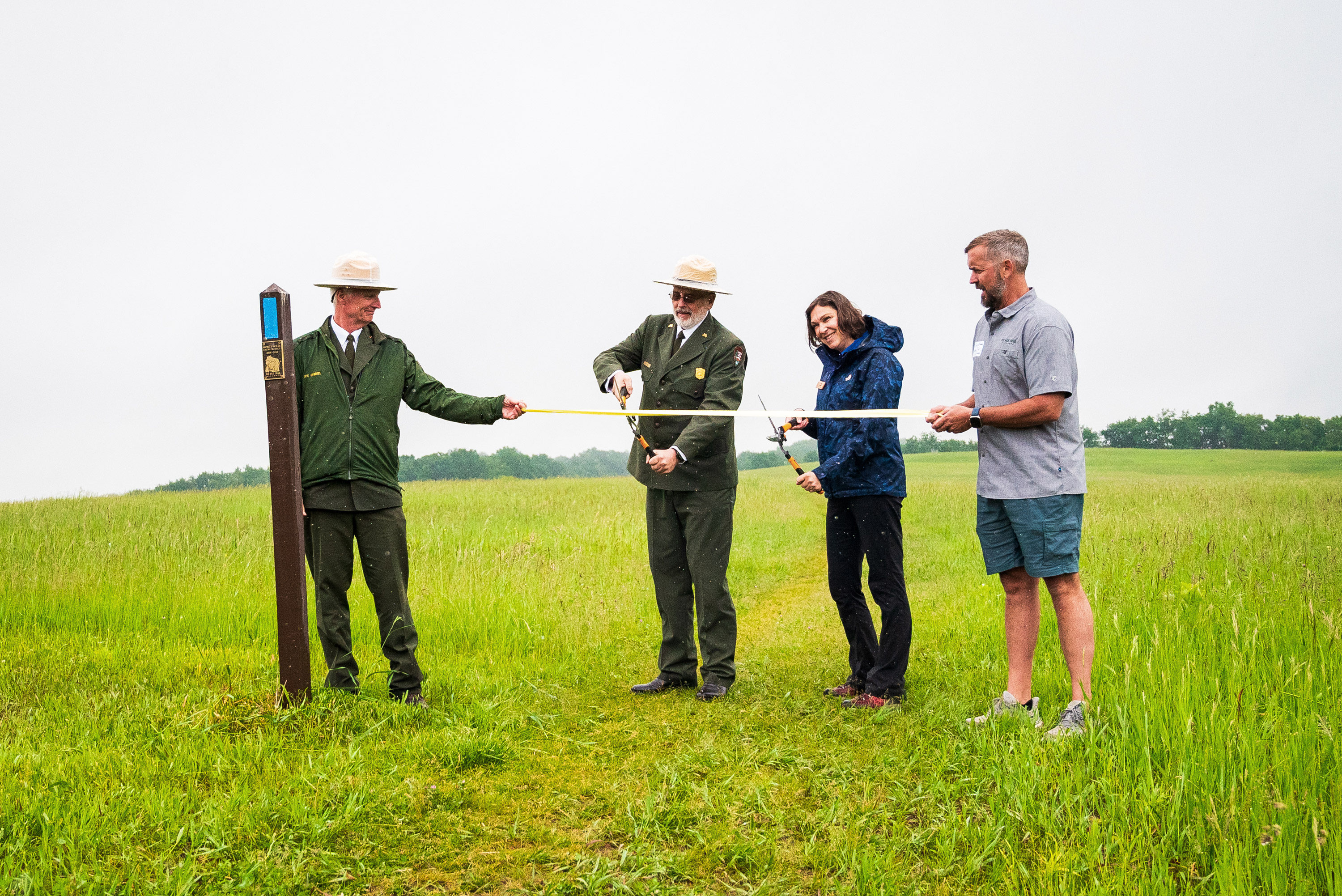 A photograph of people participating in a ribbon-cutting ceremony in a grassy field.