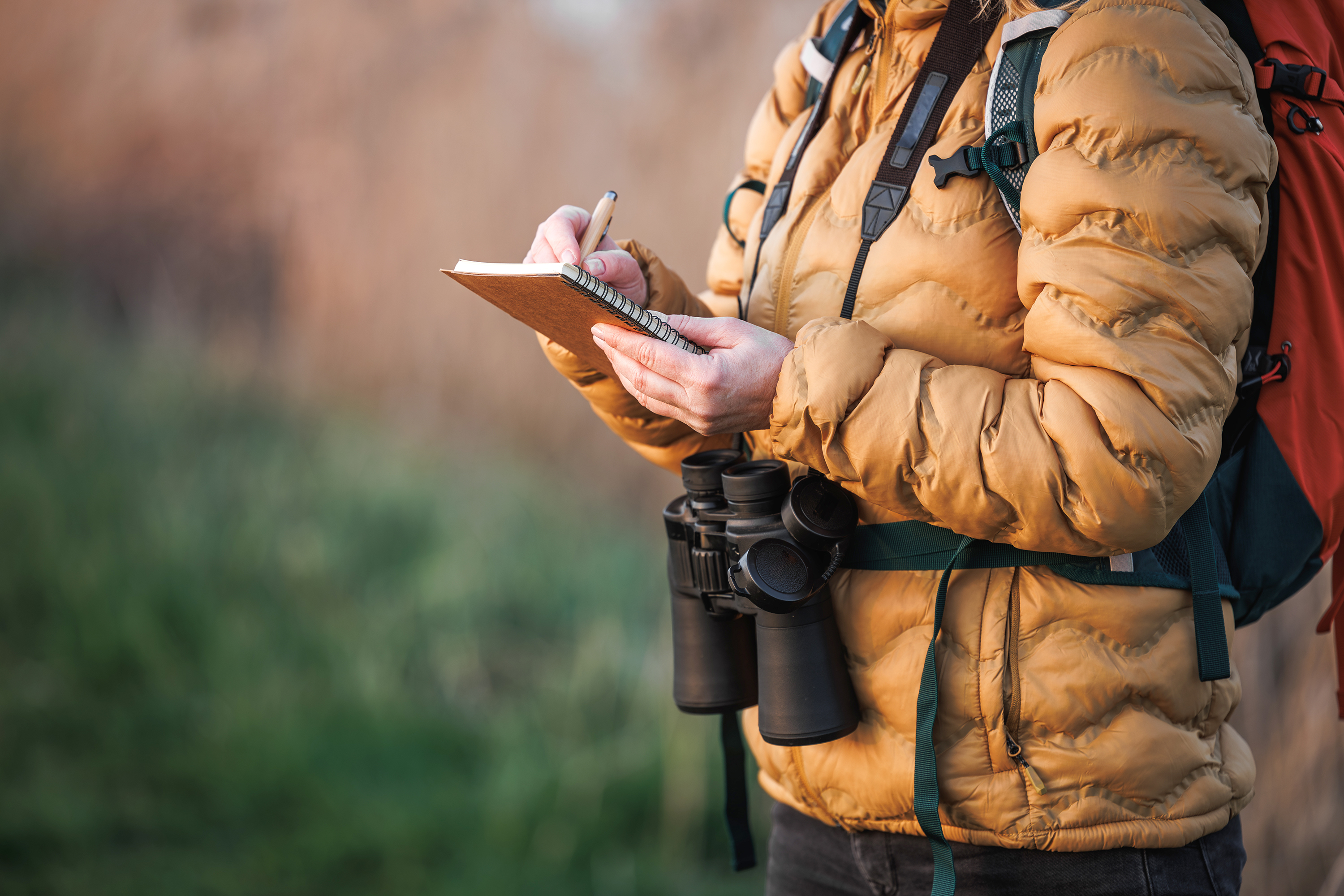 Photograph of person holding notebook with binoculars around their neck outside.