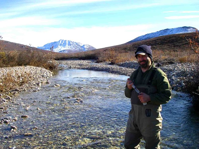 A researcher collects water samples on an Arctic stream.