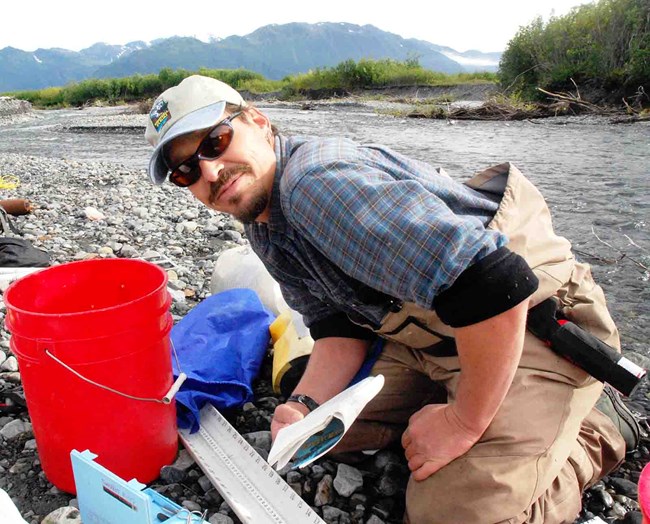 A scientist by the side of a stream collecting data.