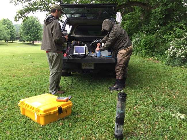 Preparing water quality monitoring equipment Two scientists removing water quality monitoring devices from the back of a vehicle parked at a field site.