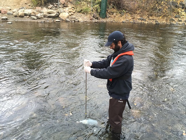 a man holds a steel rod down into the current of a river