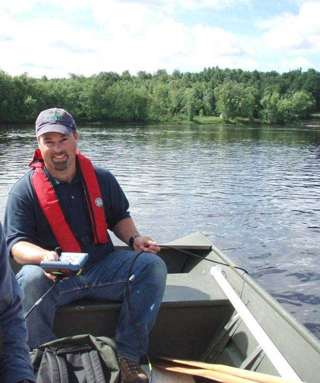 a man in a green boat holds a small computer screen in one hand and a cord over the side