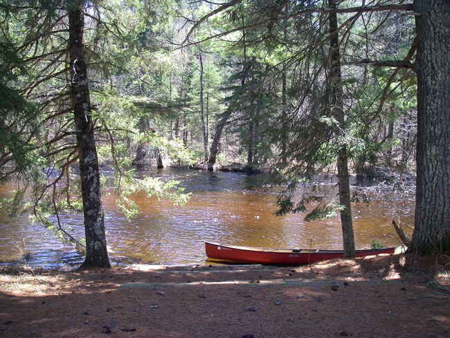 A red canoe on the bank of a wooded river