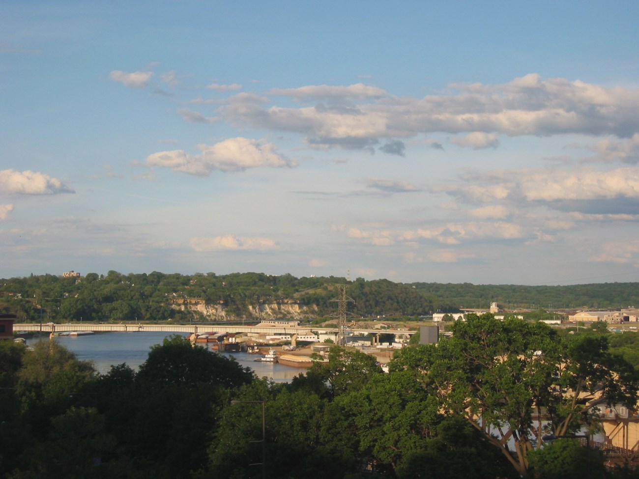 MISS_St. Paul Buildings, pavement, and a bridge lie along and over the Mississippi River. Green trees are visible in the foreground and on the horizon beyond the road bridge.