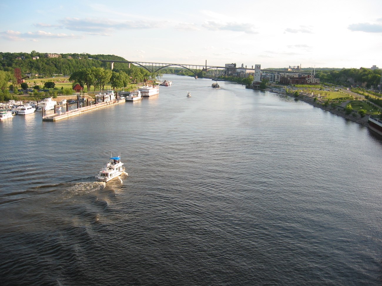 IMG_0031 Boats move along a river lined with grassy parks, buildings, and a road bridge.