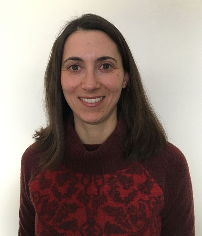 a smiling woman stands against a blank wall