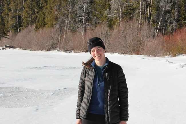 a woman stands in the snow with a forest behind her